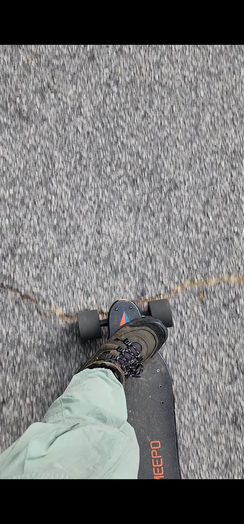 A first-person view of one foot riding an electric skateboard along a road.